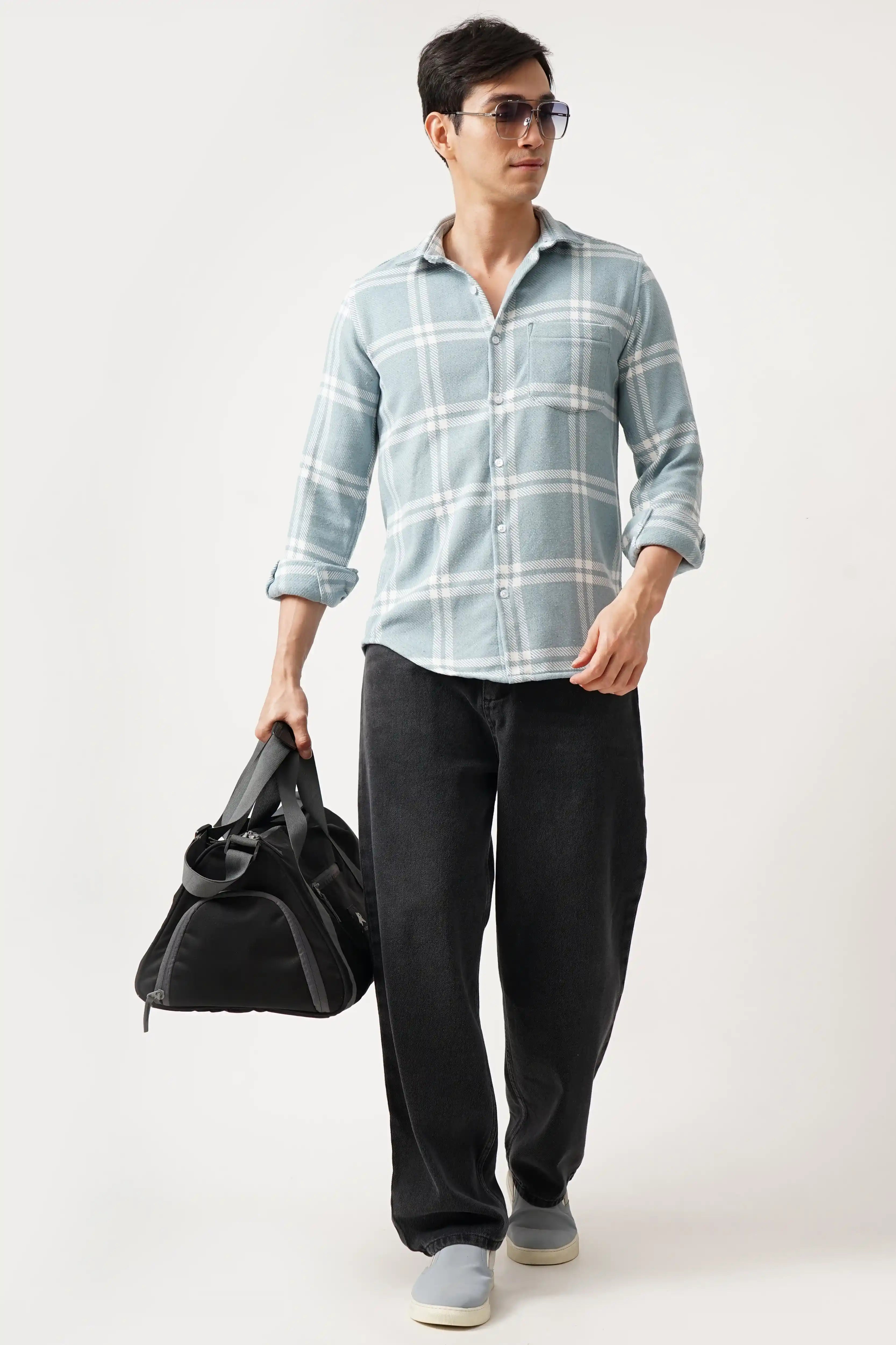 Man wearing GRIDLUX BRUSH CHECK SHIRT, light blue with timeless check pattern, paired with dark pants and carrying a black bag.