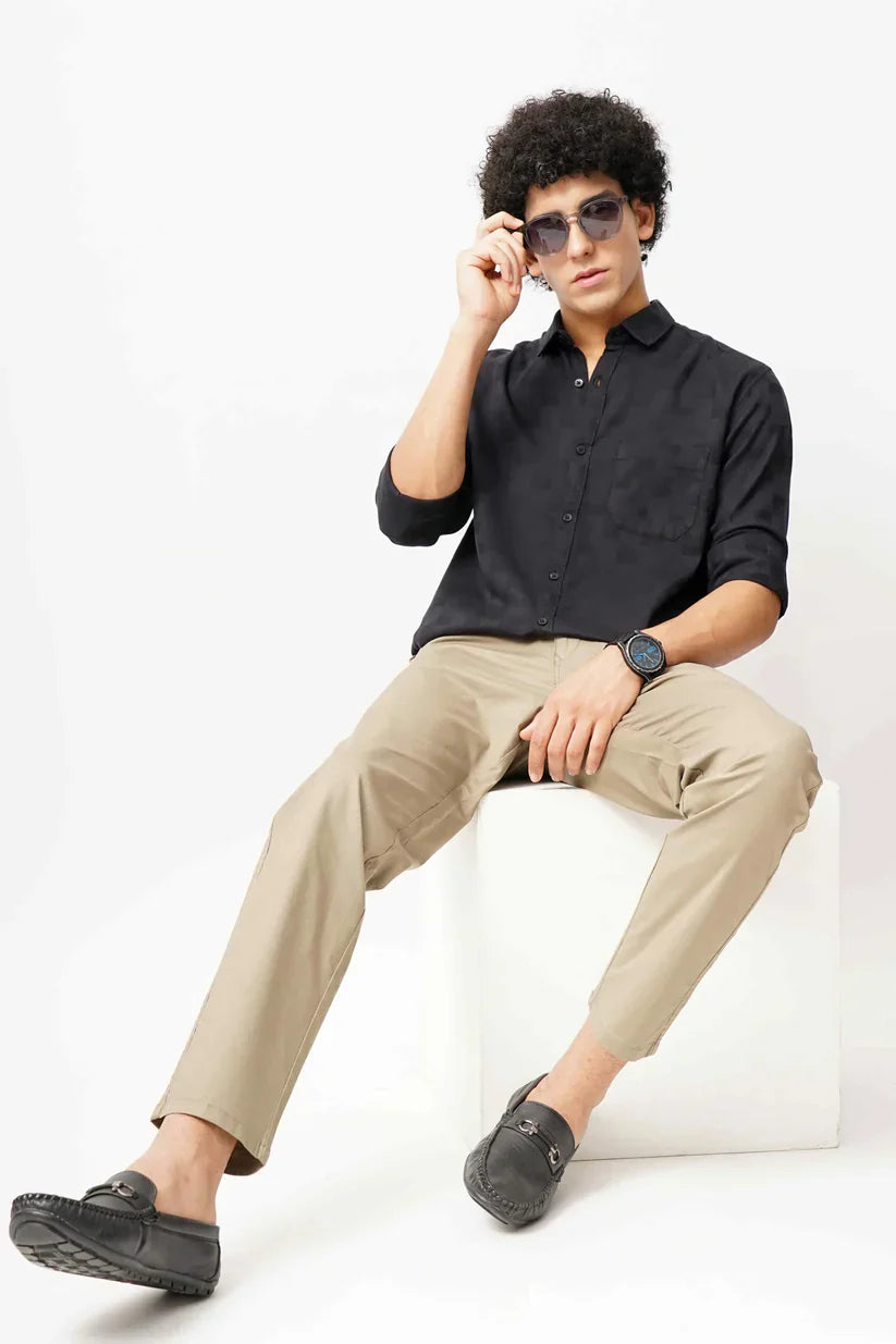 Man wearing a stylish black jacquard shirt sitting on a white cube.