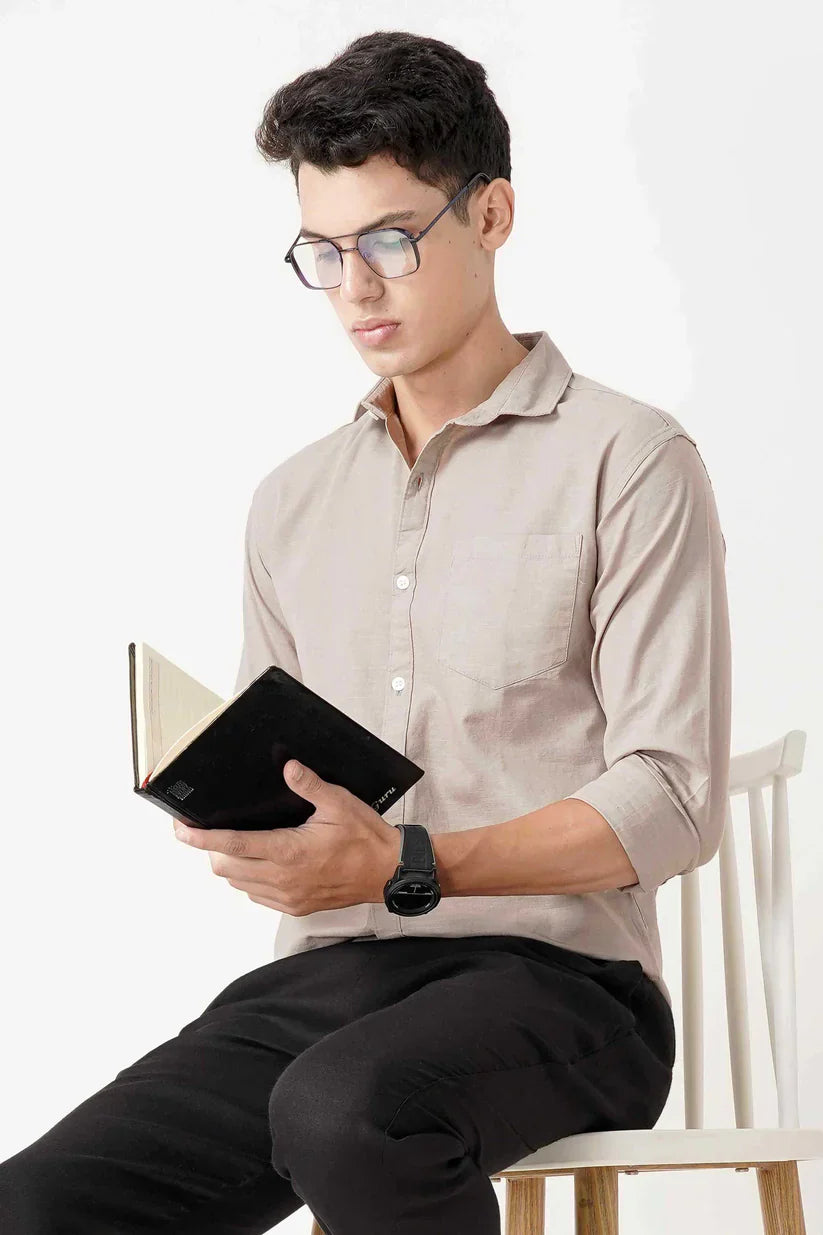 Man wearing beige linen shirt while reading a book.