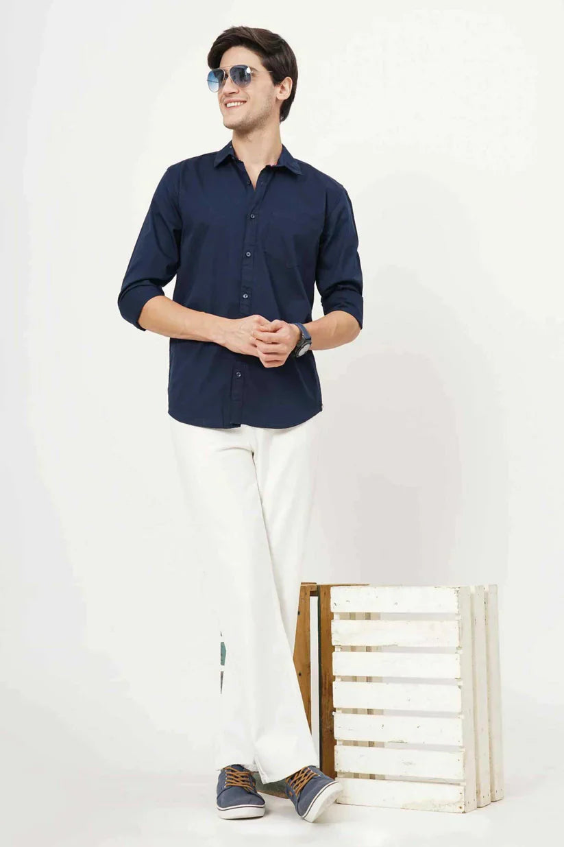 Man wearing blueish plain shirt, cotton fabric, white pants, and sunglasses.