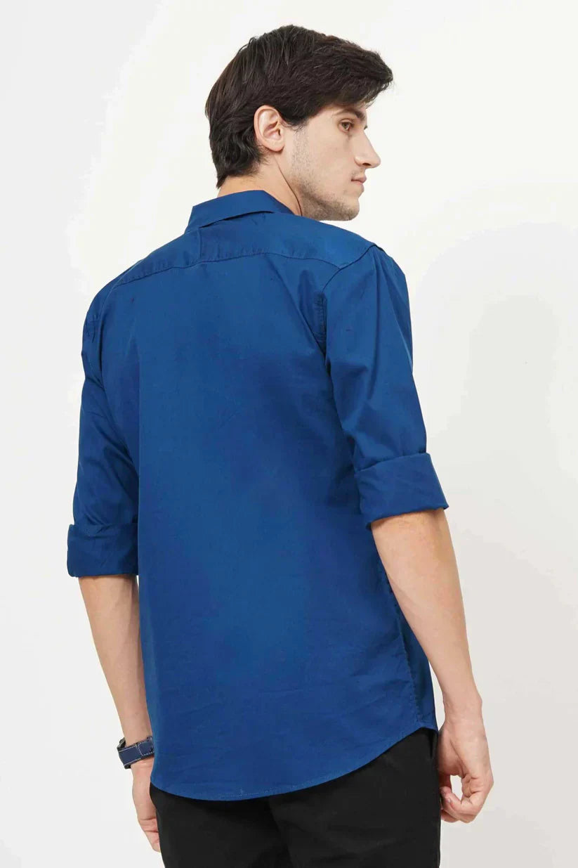 Rear view of a man in a blue plain shirt with rolled-up sleeves.