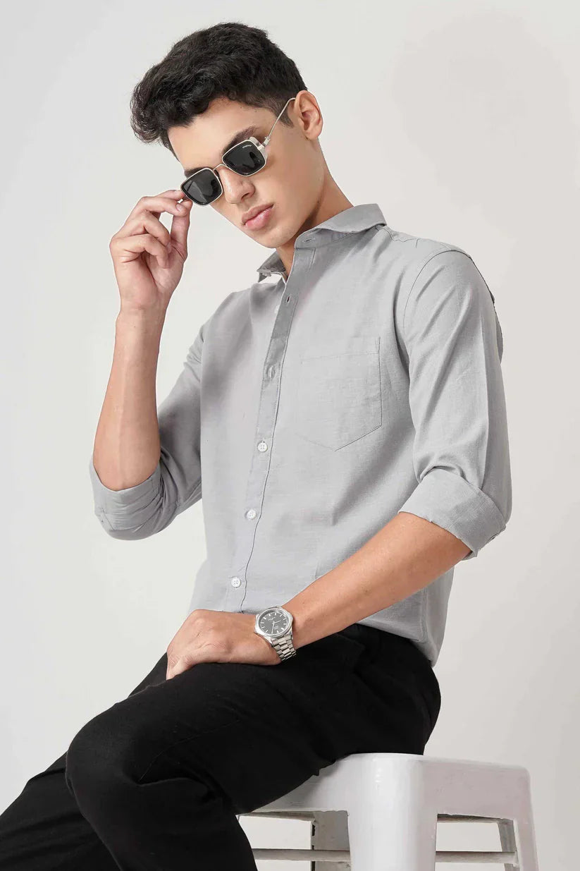 Man wearing an ice blue linen shirt, sitting and adjusting sunglasses.